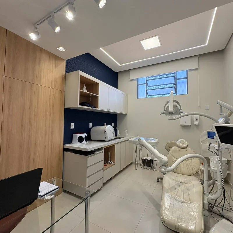 Consultório com painel amadeirado, parede azul e cadeira odontológica